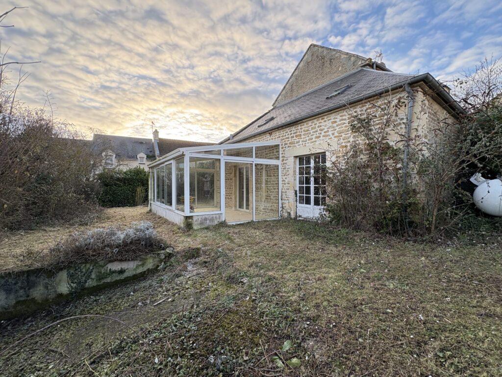 Maison en pierre avec véranda vitrée et jardin à rénover au coucher du soleil