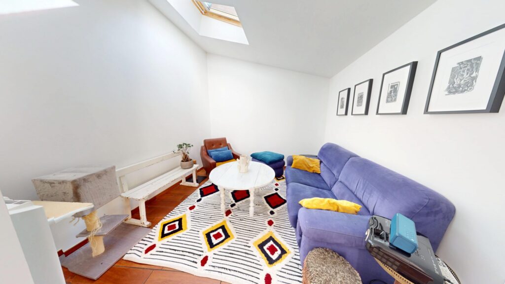 Salon lumineux avec canapé violet, tapis géométrique et puits de lumière sous toit