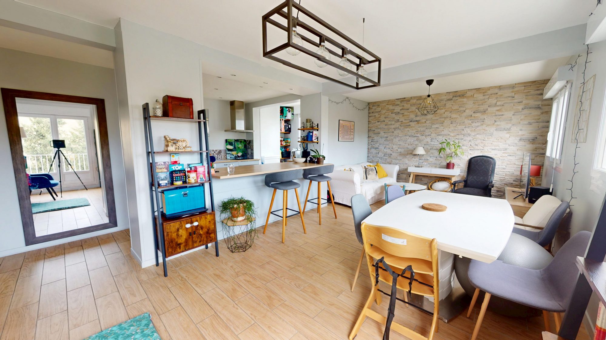 Séjour lumineux avec cuisine ouverte, îlot, salle à manger et mur en pierre