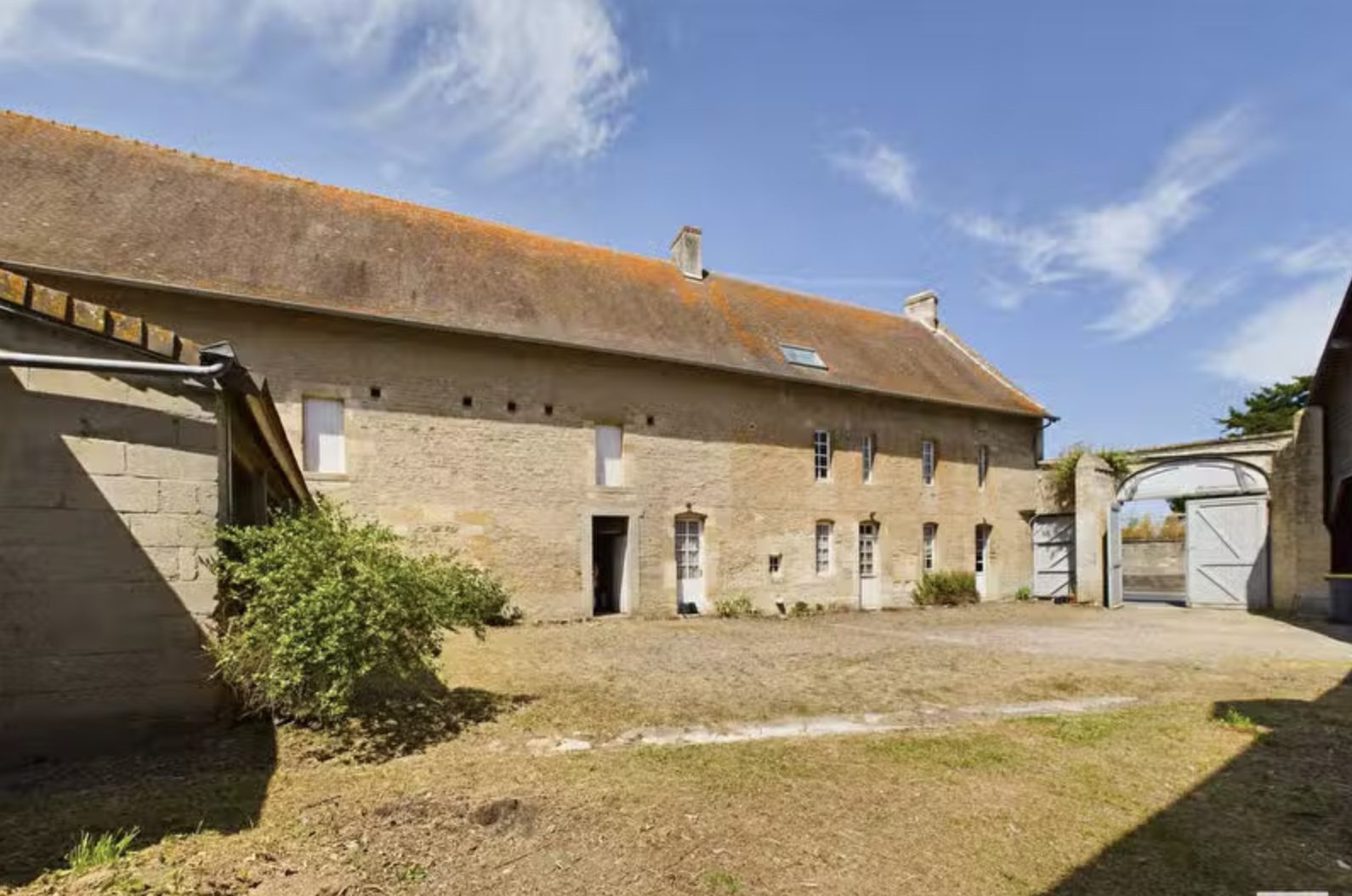 Cour intérieure d'une ferme en pierre avec portail voûté et toit en tuiles sous ciel bleu