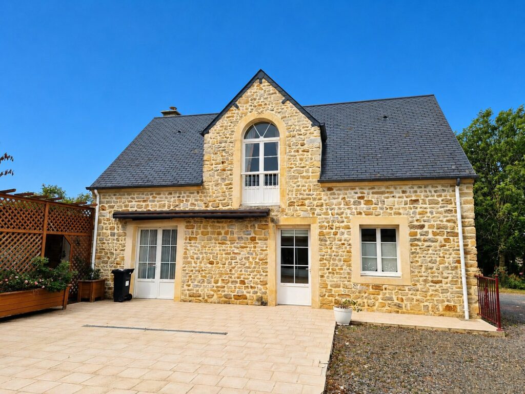 Maison en pierre avec toiture en ardoise et cour pavée sous ciel bleu