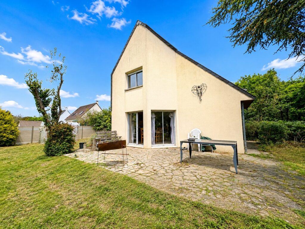 Maison contemporaine crépie avec terrasse en pierre et grand jardin verdoyant sous ciel bleu