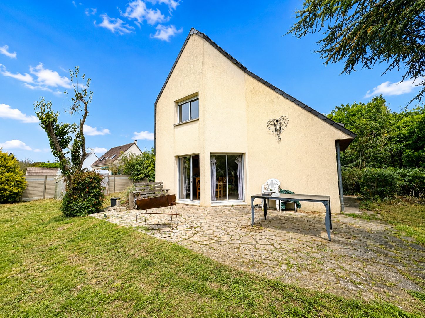 Maison contemporaine crépie avec terrasse en pierre et grand jardin verdoyant sous ciel bleu