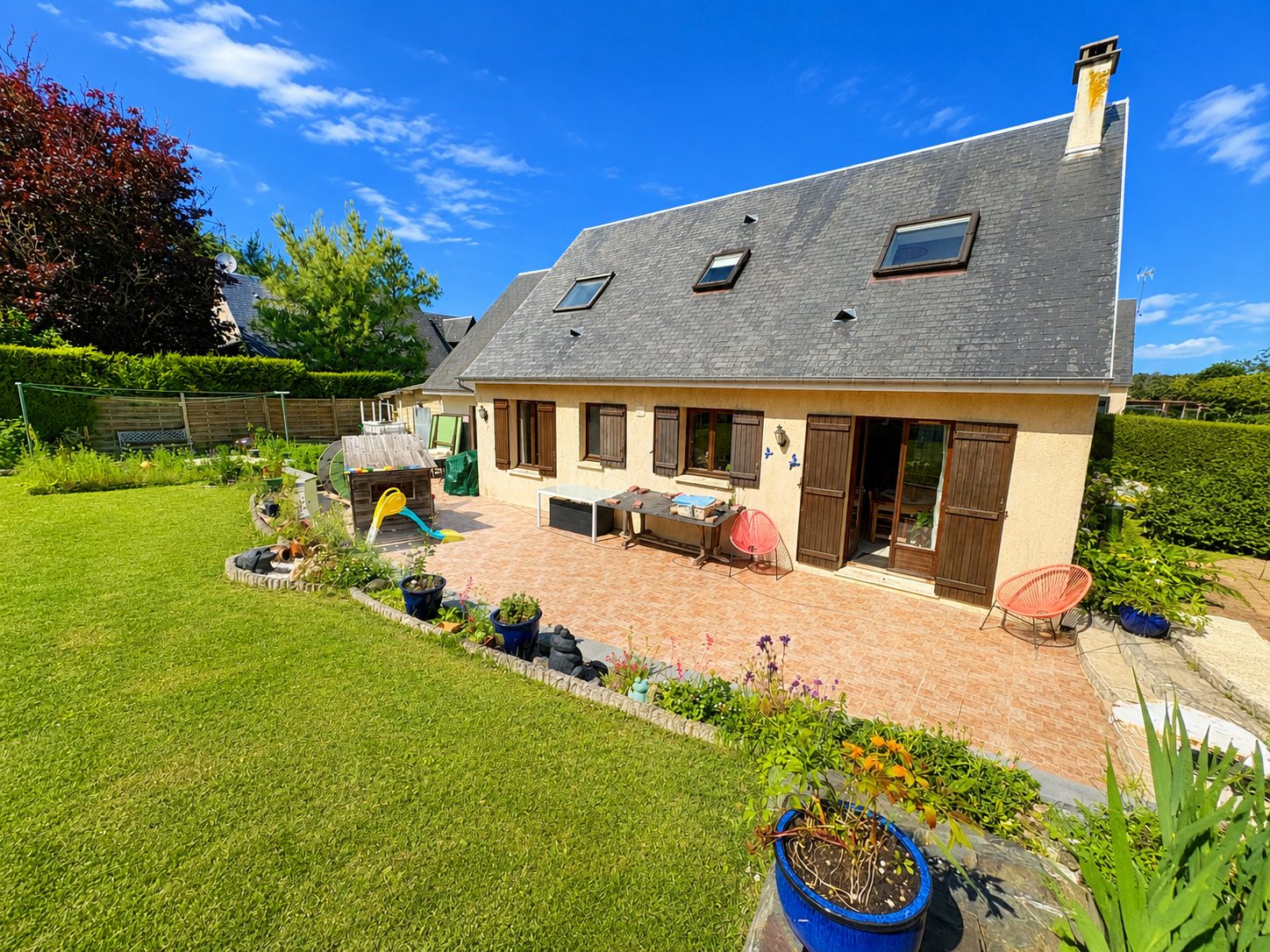 Maison individuelle à toit ardoise, terrasse carrelée et grand jardin paysager
