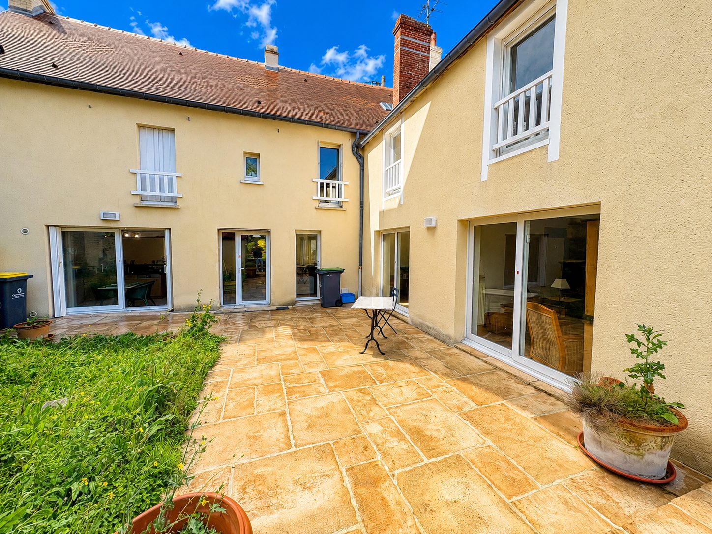 Grande terrasse en pierre d'une maison avec baies vitrées donnant sur une cour ensoleillée