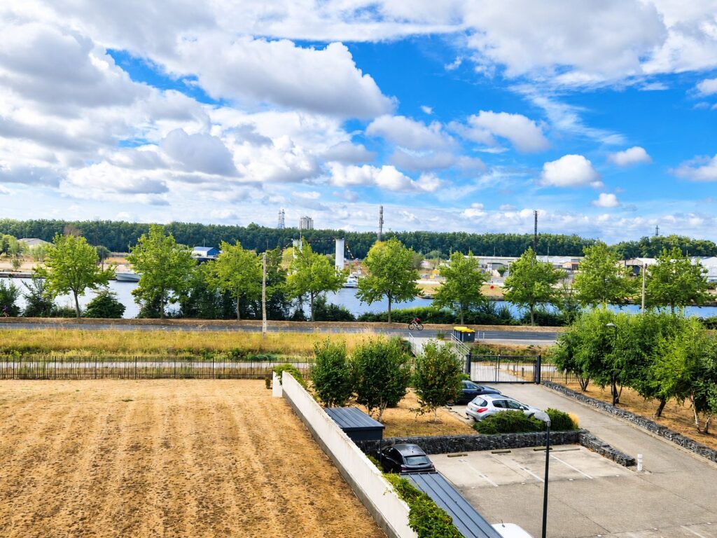 Vue panoramique d’un parking arboré et d’une rivière sous un ciel bleu nuageux