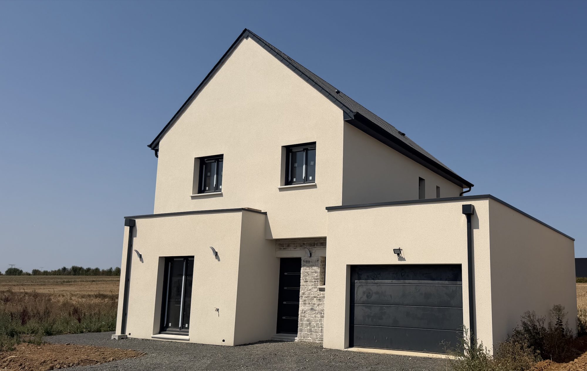 Maison contemporaine crépie beige avec garage intégré et menuiseries noires sous ciel bleu