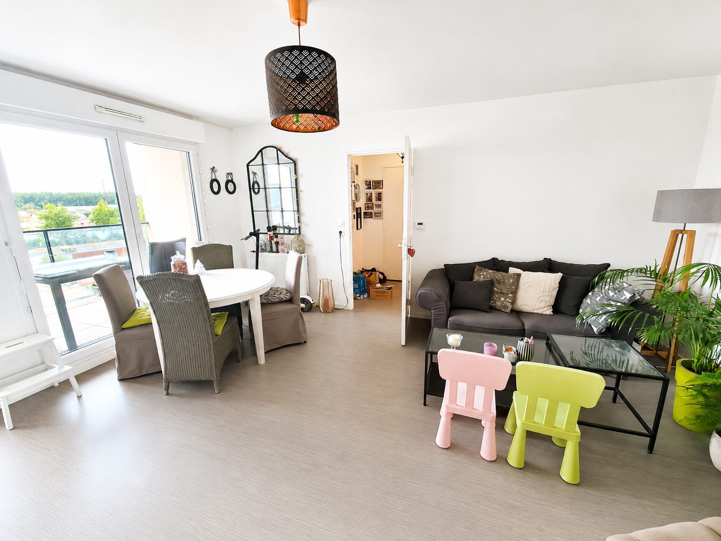 Salon-salle à manger lumineux avec balcon, canapé gris, table ronde et chaises enfant colorées